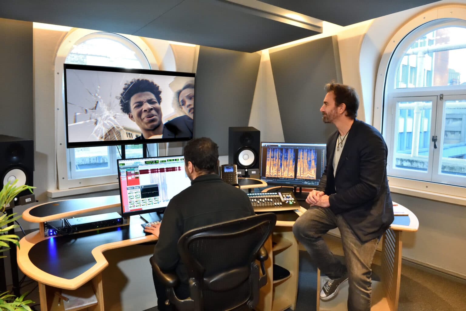 Two men work in a modern studio with a large screen showing a film scene and audio equipment.